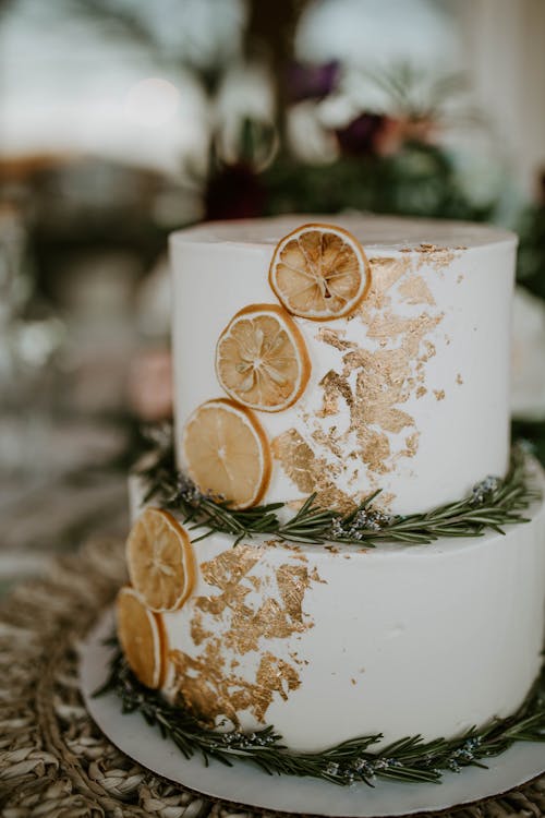 Festive two tier cake decorated with food gold and sliced dried oranges with rosemary twigs on table for wedding celebration