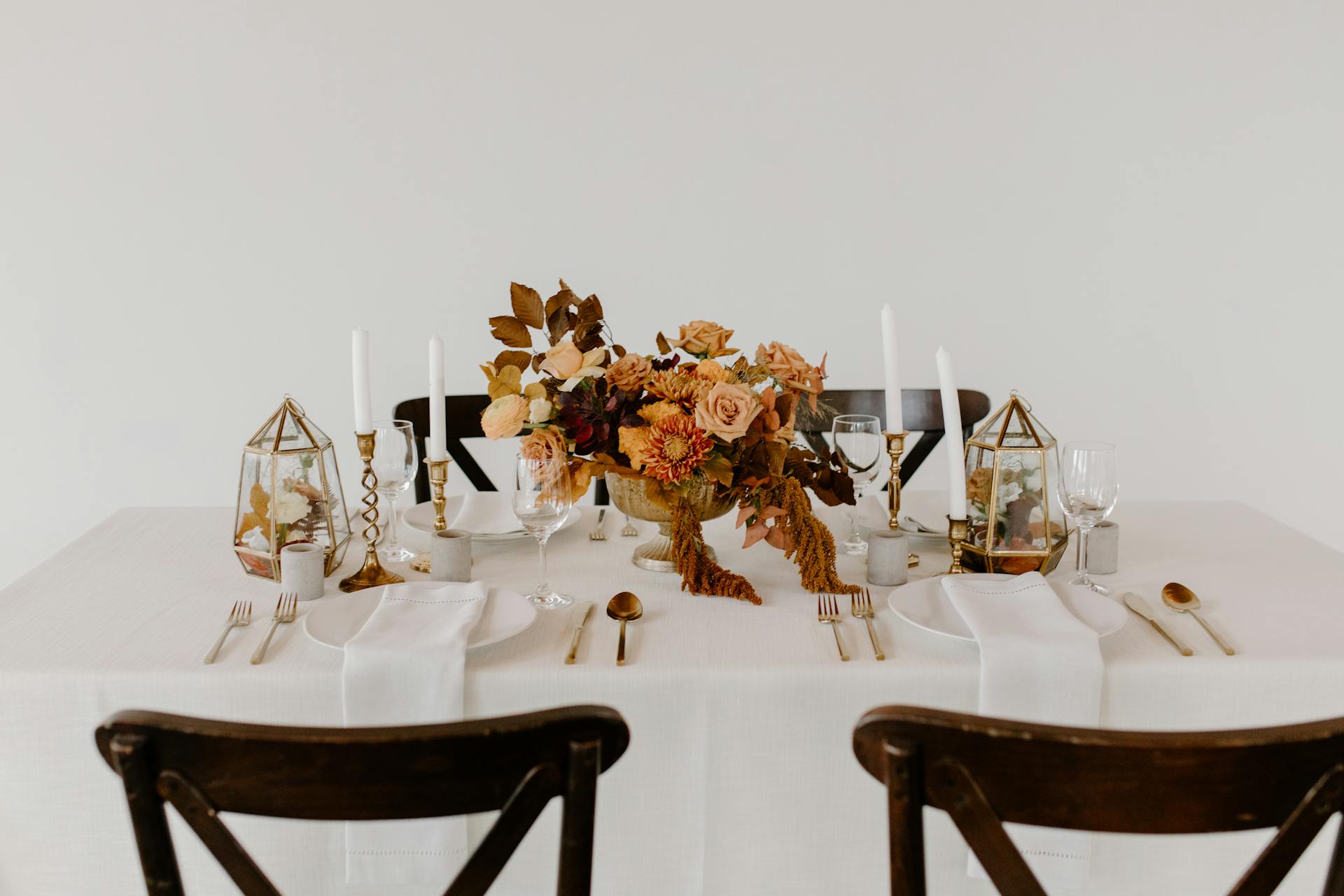 Set of dishware and cutlery placed on table decorated with candles and blooming flowers for wedding celebration