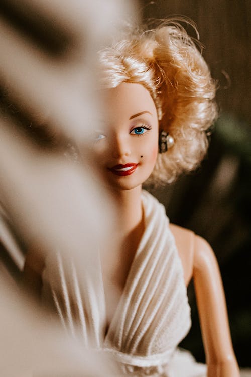 Smiling doll with blond curly hairstyle wearing elegant white decollete dress for wedding