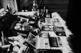 Black and white high angle of assorted makeup products and tools placed on dressing table near mirror