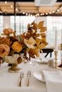 Elegant floral composition in vase placed on white table with ceramic plates and golden cutlery during festive banquet