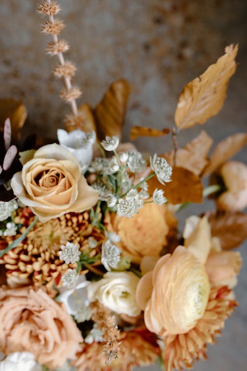 From above of delicate bouquet with peach buttercups and roses composed with chrysanthemum flowers and yellow leaves