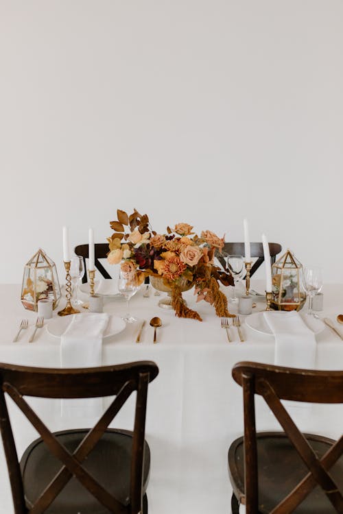 Wooden chair placed near banquet table with elegant dishware decorated with candles and floral composition against white wall