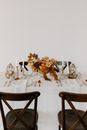 Wooden chair placed near banquet table with elegant dishware decorated with candles and floral composition against white wall