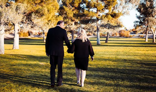 Man and Woman Walking on Green Grass Field while Holding Hands