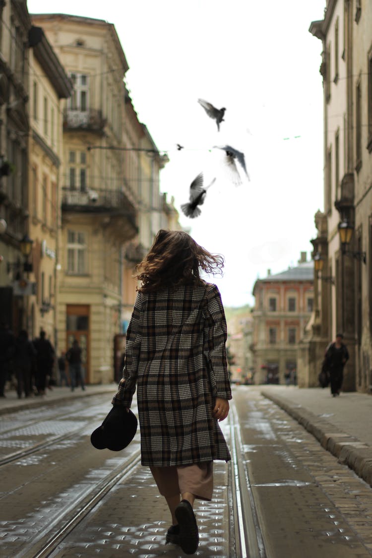 Back View Of A Woman Walking With Doves Flying In Front Of Her