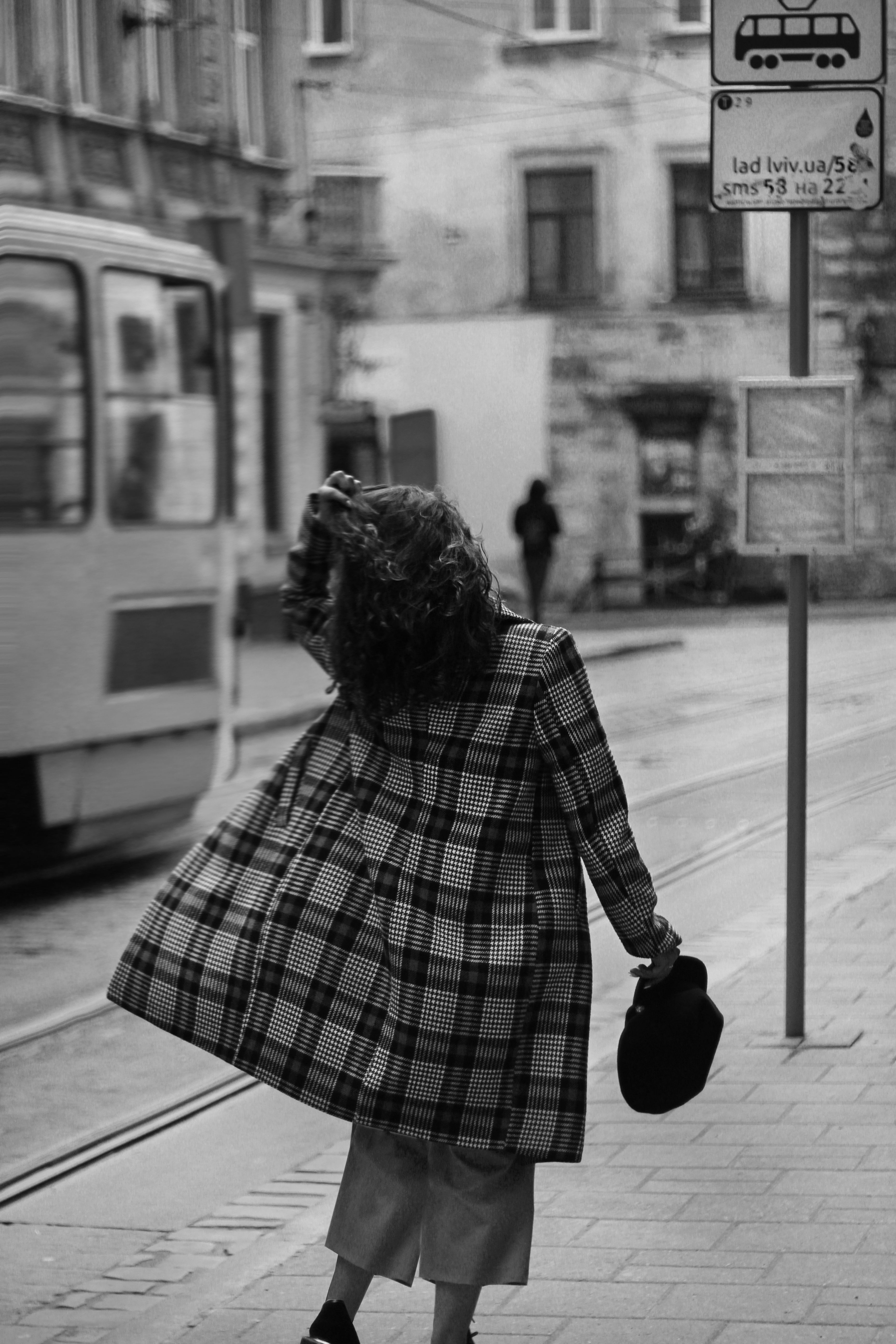 Grayscale Photo of a Woman in a Plaid Coat Walking on the Sidewalk ...