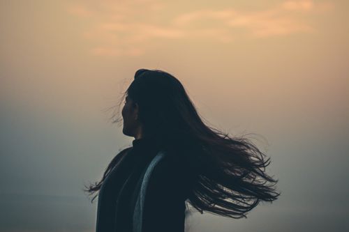 Free Side view of unrecognizable female shaking long hair while standing on shore near foggy sea on evening time in nature Stock Photo