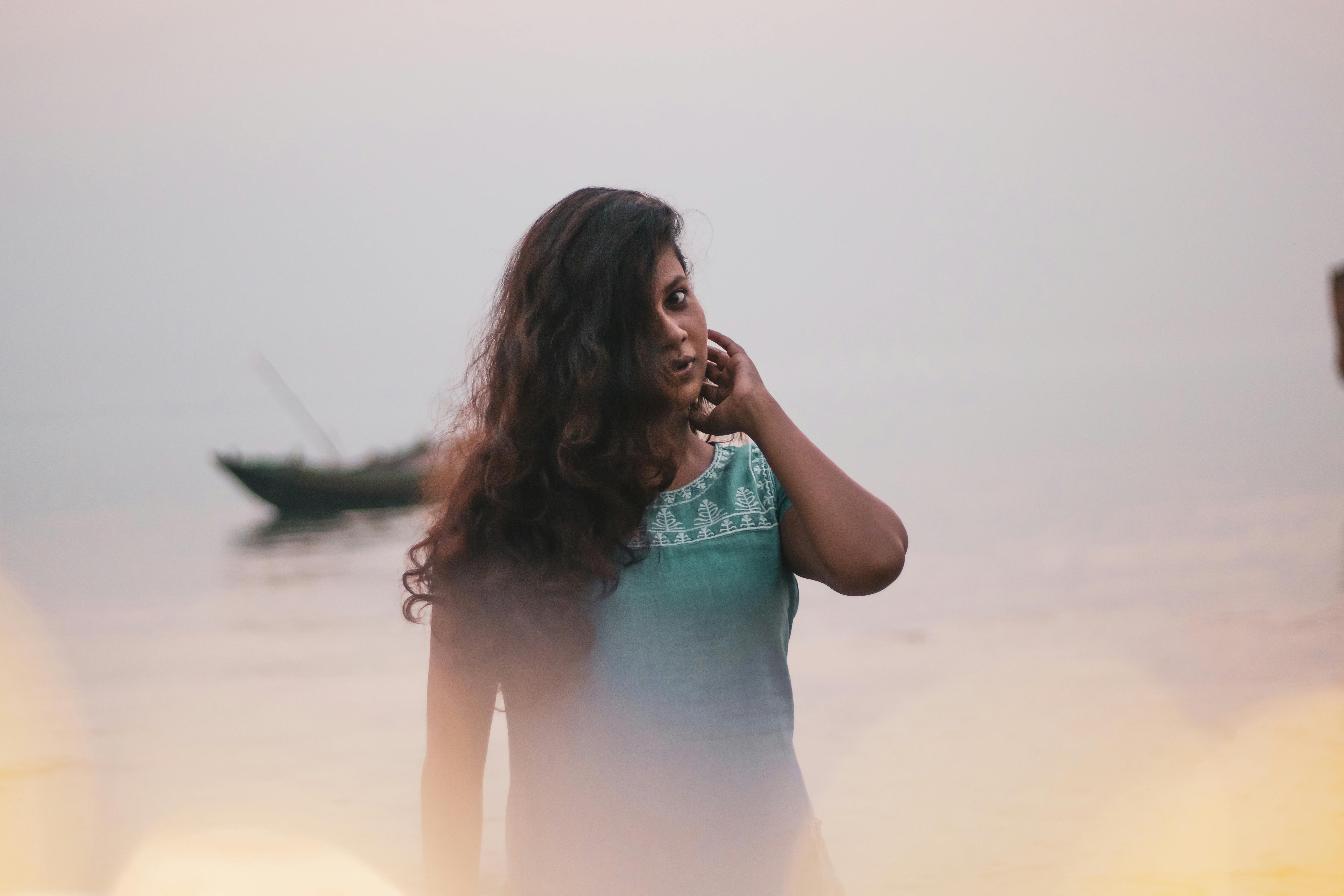 A young woman with long hair stands peacefully by the waterfront, exuding a serene and calm vibe.