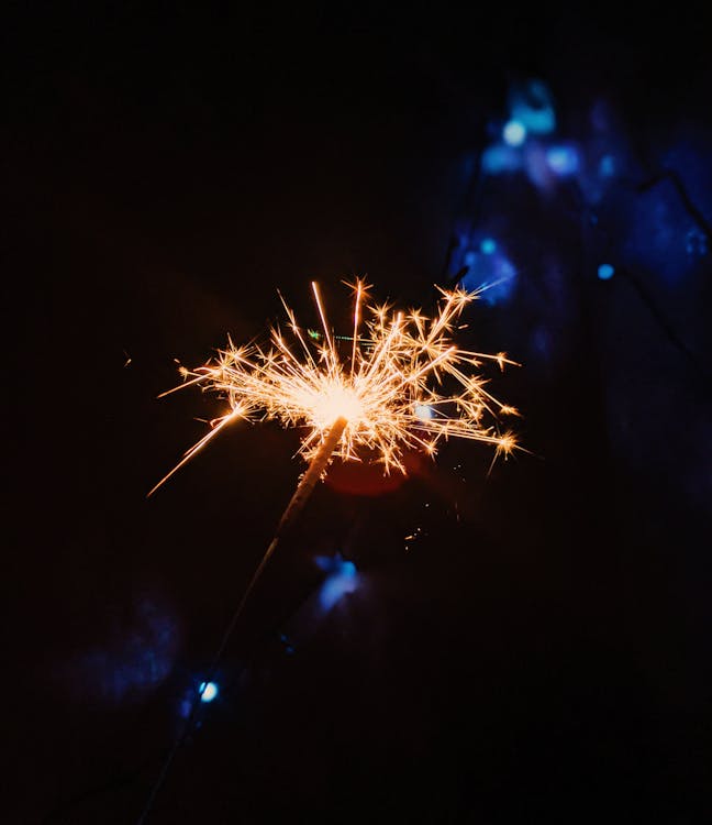 Colorful Bengal lights with sticks and bright luminous sparks burning in darkness with shadows during festive event in night time