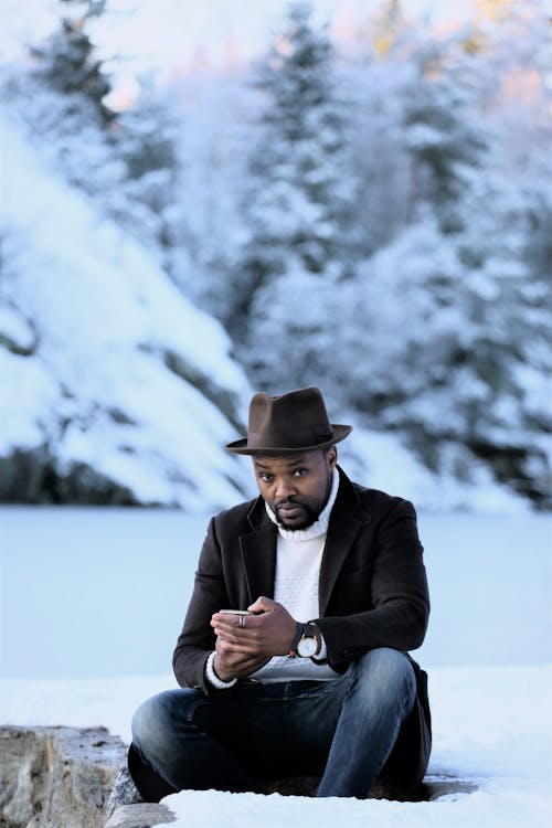 Man in Black Jacket and Black Hat Sitting on the Snow