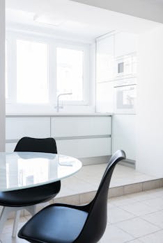 Bright modern apartment interior with glass table near chairs and windows near white counter with tap