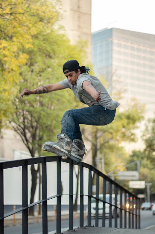 A Man in Gray Shirt Skating on Metal Railings on the Street