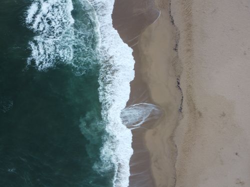Free Drone shot capturing the stunning waves meeting the sandy shore in Punta del Este, Uruguay. Stock Photo
