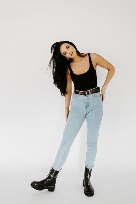 A fashionable woman posing in a black tank top and light jeans in a studio photoshoot.