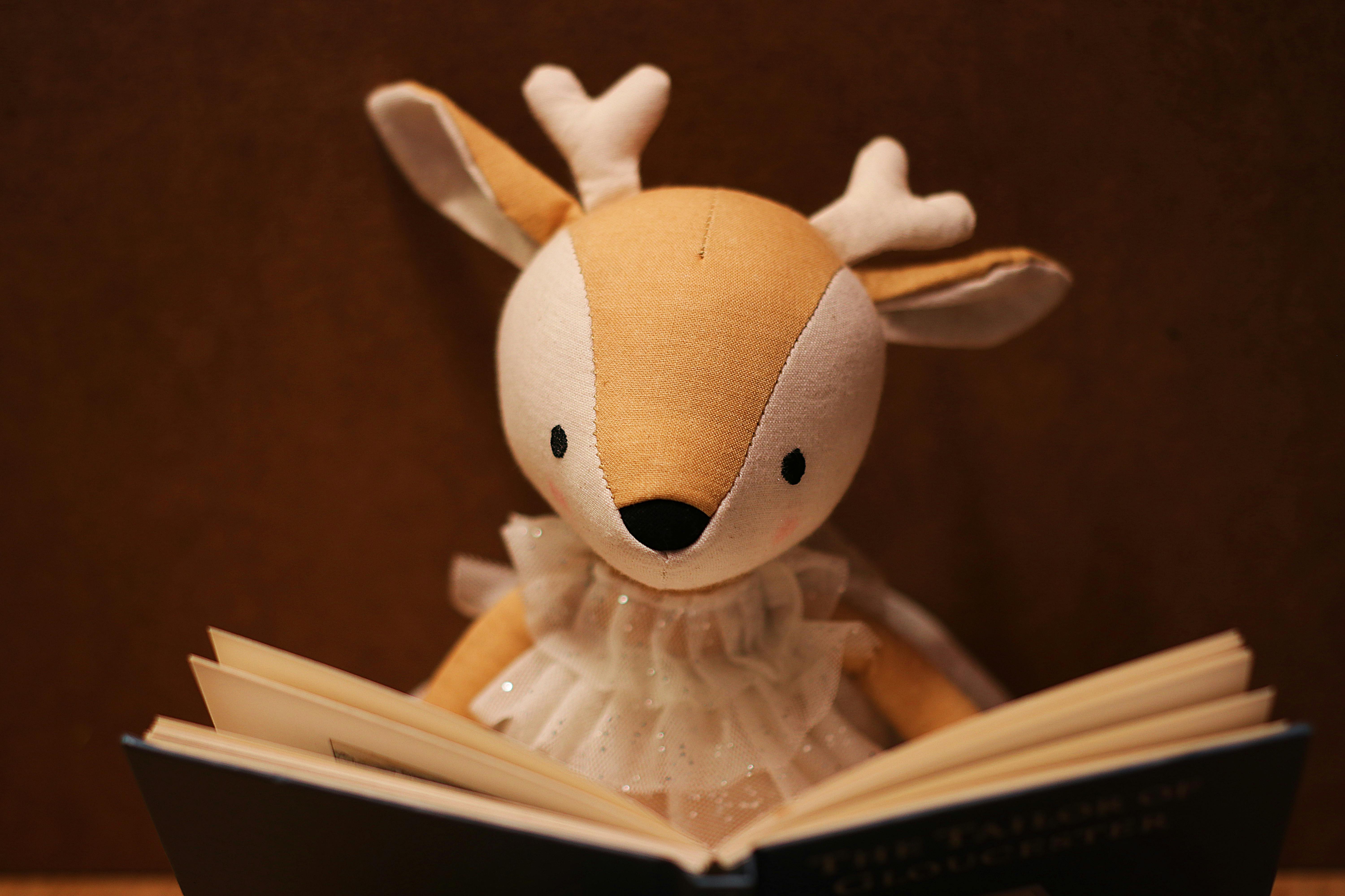 A cute plush deer toy engrossed in reading a book, symbolizing curiosity and education.