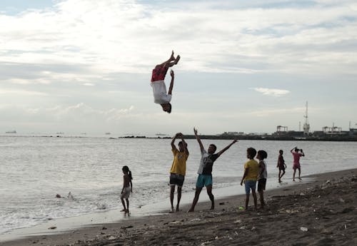 Free Man in White Shirt and Red Shorts Doing Backflip near Beach Stock Photo