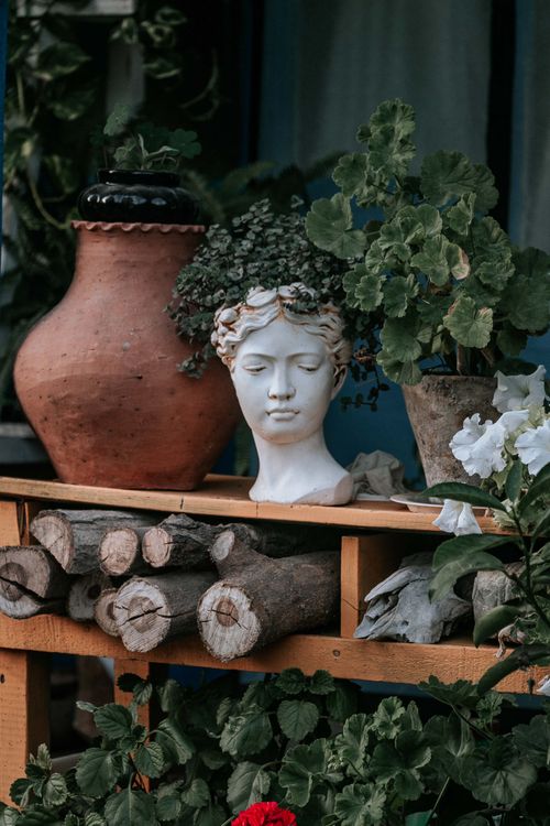 Free A serene garden arrangement featuring a classical bust, clay pot, and lush foliage. Stock Photo