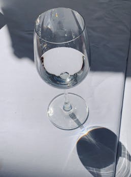 An artistic shot of a wine glass with water and sunlight reflection on a white surface.
