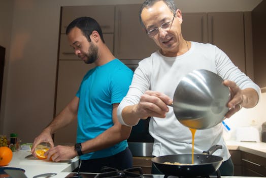 Two men cooking together in a well-lit modern kitchen, sharing a moment of togetherness and culinary creativity.