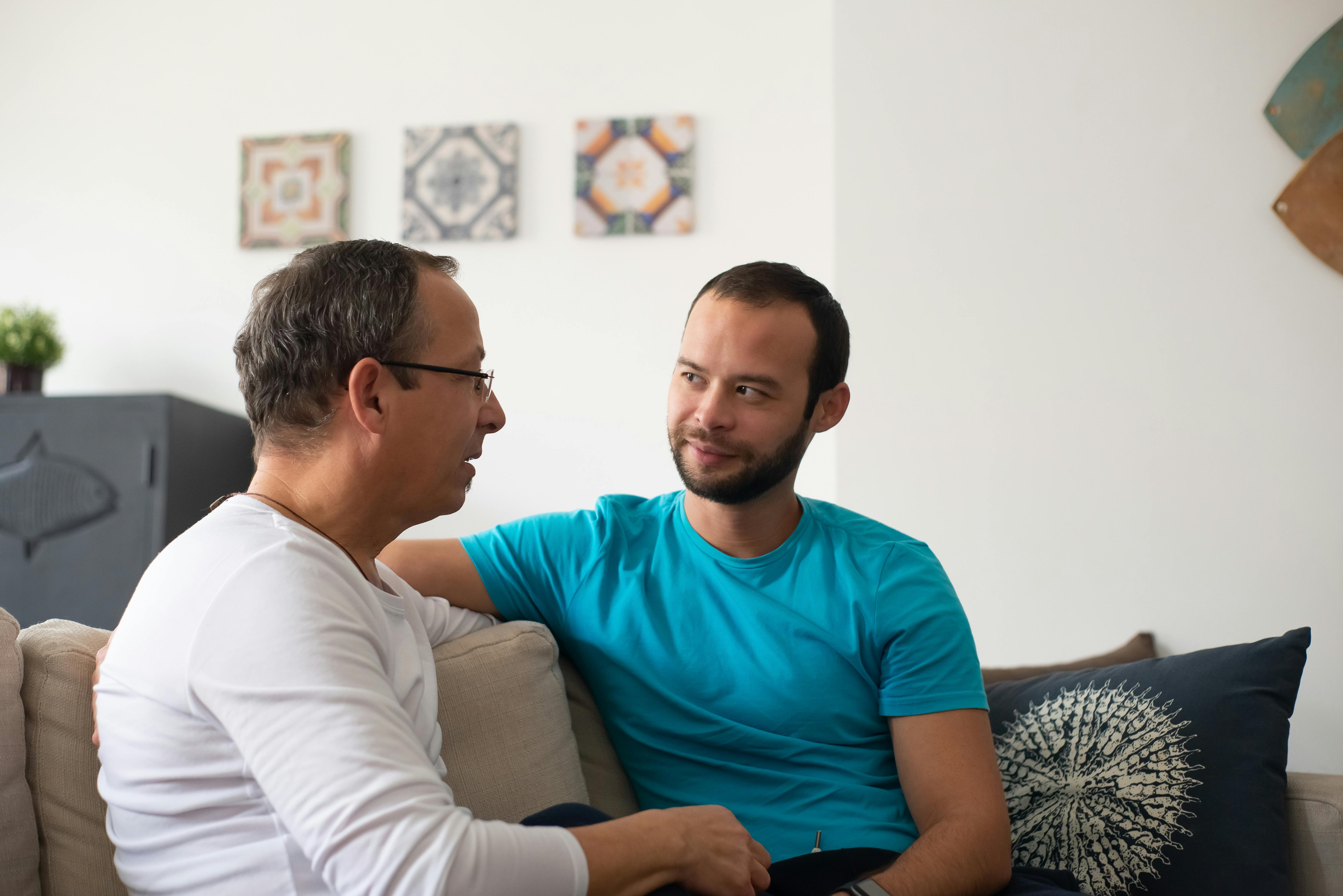 Two men share a heartfelt conversation on a cozy sofa in a modern living room.