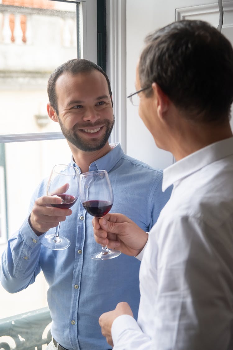 Two Men Looking At Each Other Clinking Glasses With Red Wine