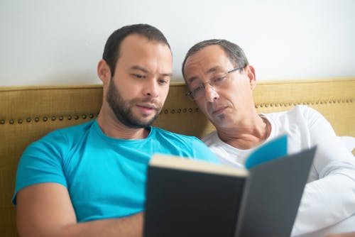 Free Two Men Reclining On Bed Looking at a Book Stock Photo