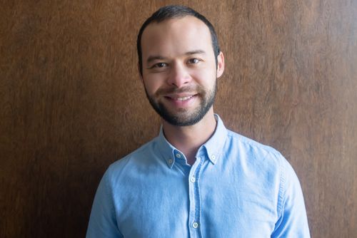 Free A portrait of a smiling man wearing a blue shirt standing against a wooden background indoors. Stock Photo
