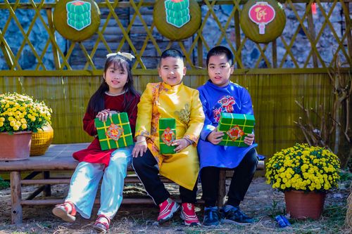 Free Three children in traditional Vietnamese clothing sit with festive packages, celebrating Tet. Stock Photo