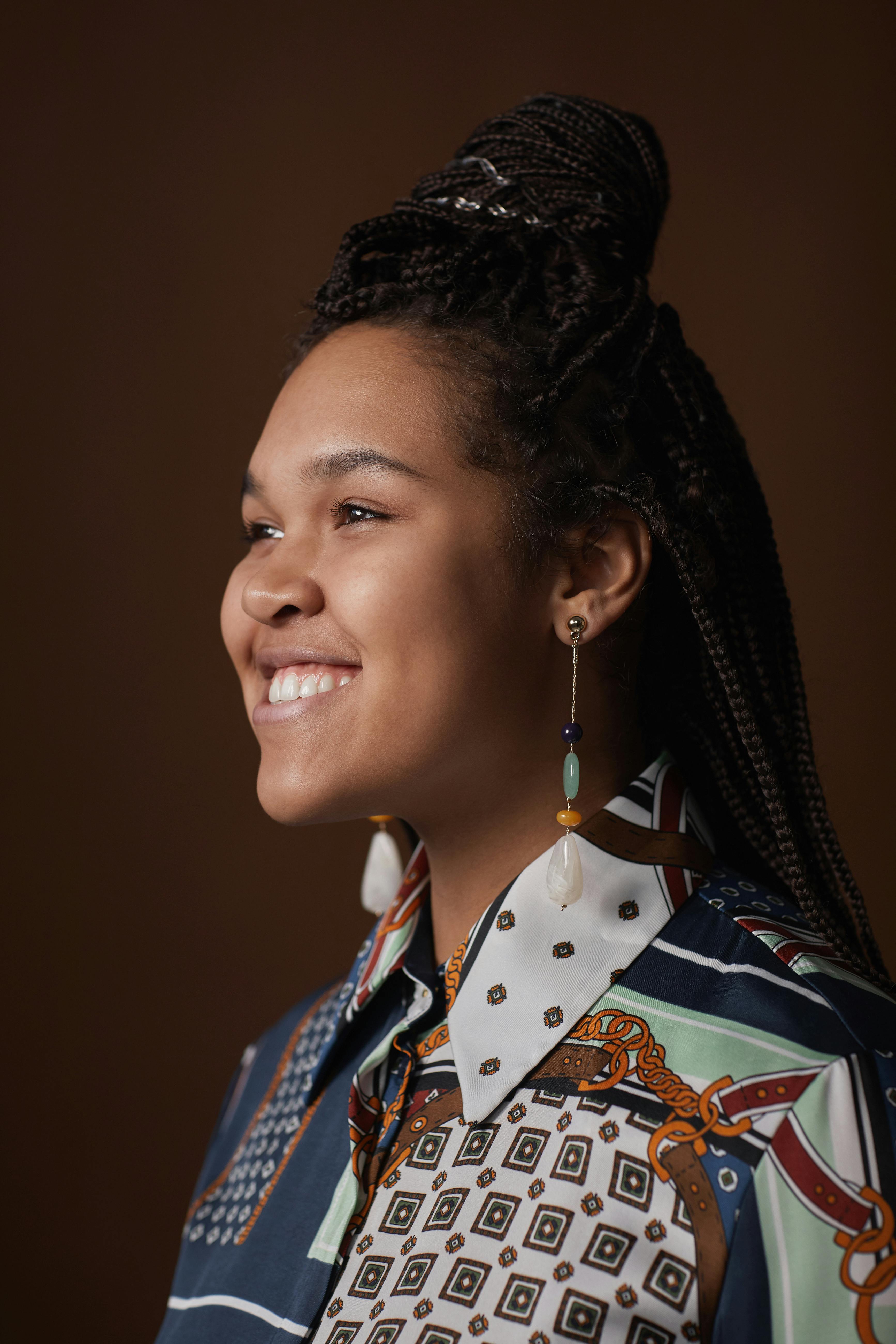 Portrait of a happy woman with braided hair wearing a patterned blouse, smiling in a studio setting.