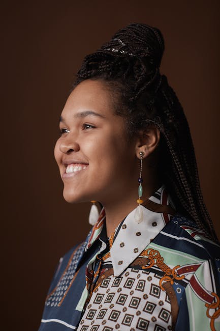 Portrait of a happy woman with braided hair wearing a patterned blouse, smiling in a studio setting.