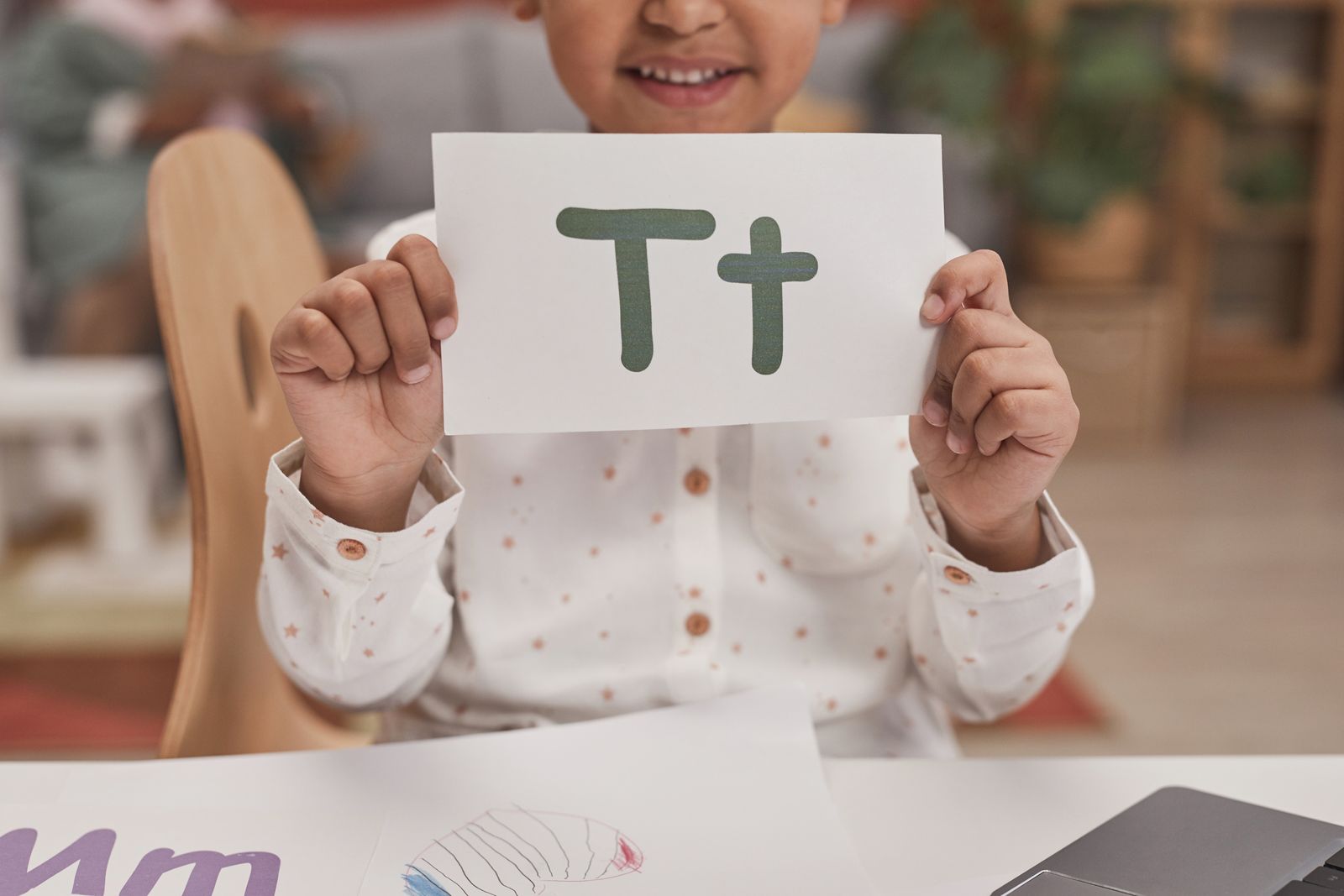 A young child holding an alphabet card during a playful early literacy lesson