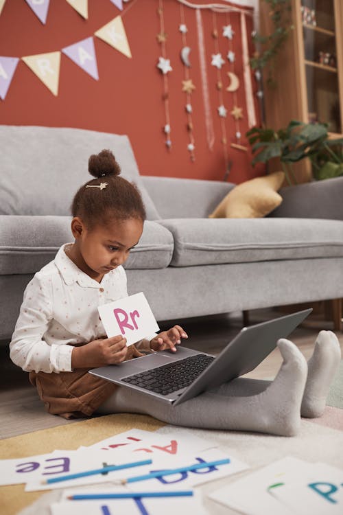 A Girl Using a Laptop while Holding an Alphabet Card