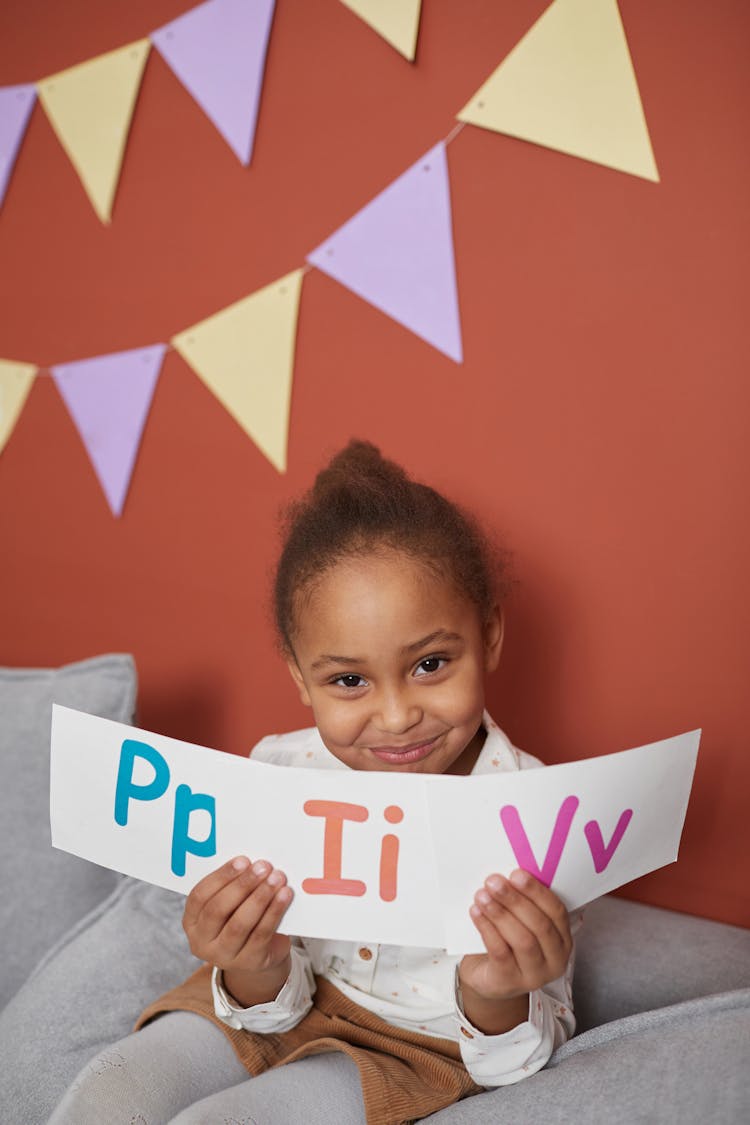 A Girl Holding Alphabet Cards While Looking At Camera