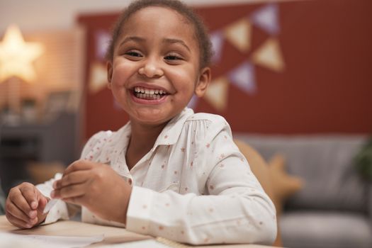 A cheerful child with a bright smile sitting at a table indoors, creating a warm and happy atmosphere.