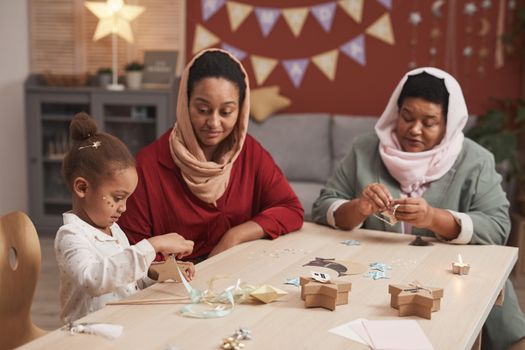 Family crafting session with three generations creating paper decorations indoors.