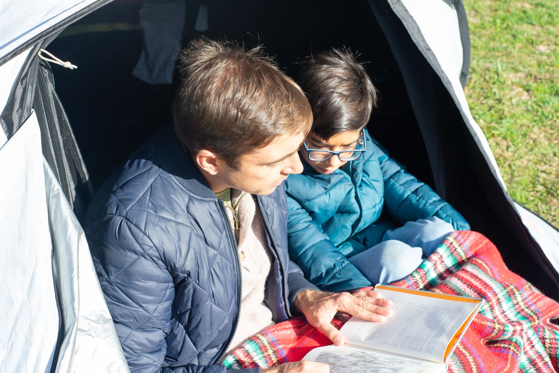 Dad reading with his son inside a tent, the kind of small ritual that builds easy conversation