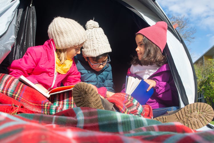 Children In Winter Clothes Sitting Inside A Tent Reading Books