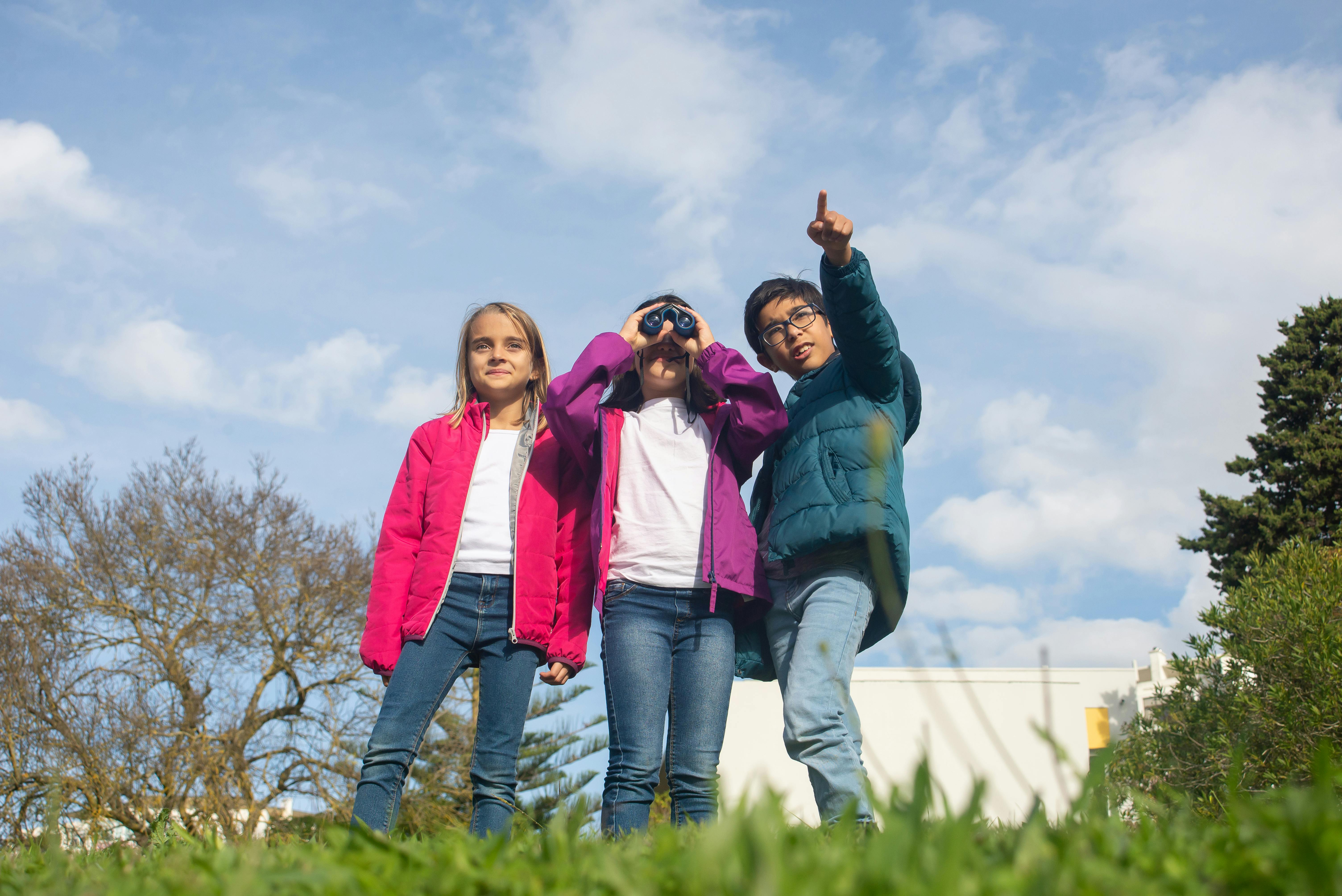 a girl holding a binoculars and a boy pointing where to look at