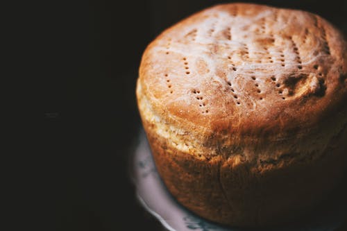 From above of delicious homemade fresh baked loaf of bread with patterns on top served on plate on blurred black background