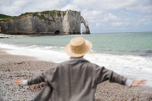 Unrecognizable traveler in hat on shore near wavy sea