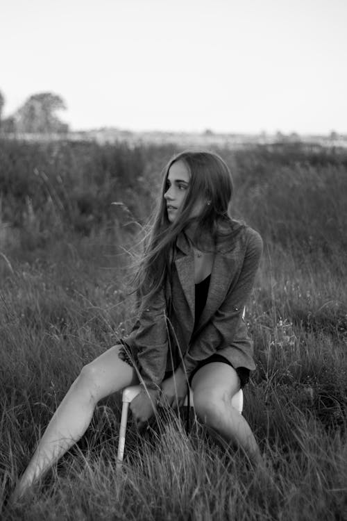 Free Monochrome Photo of a Woman Sitting on a Chair in the Middle of a Field Stock Photo