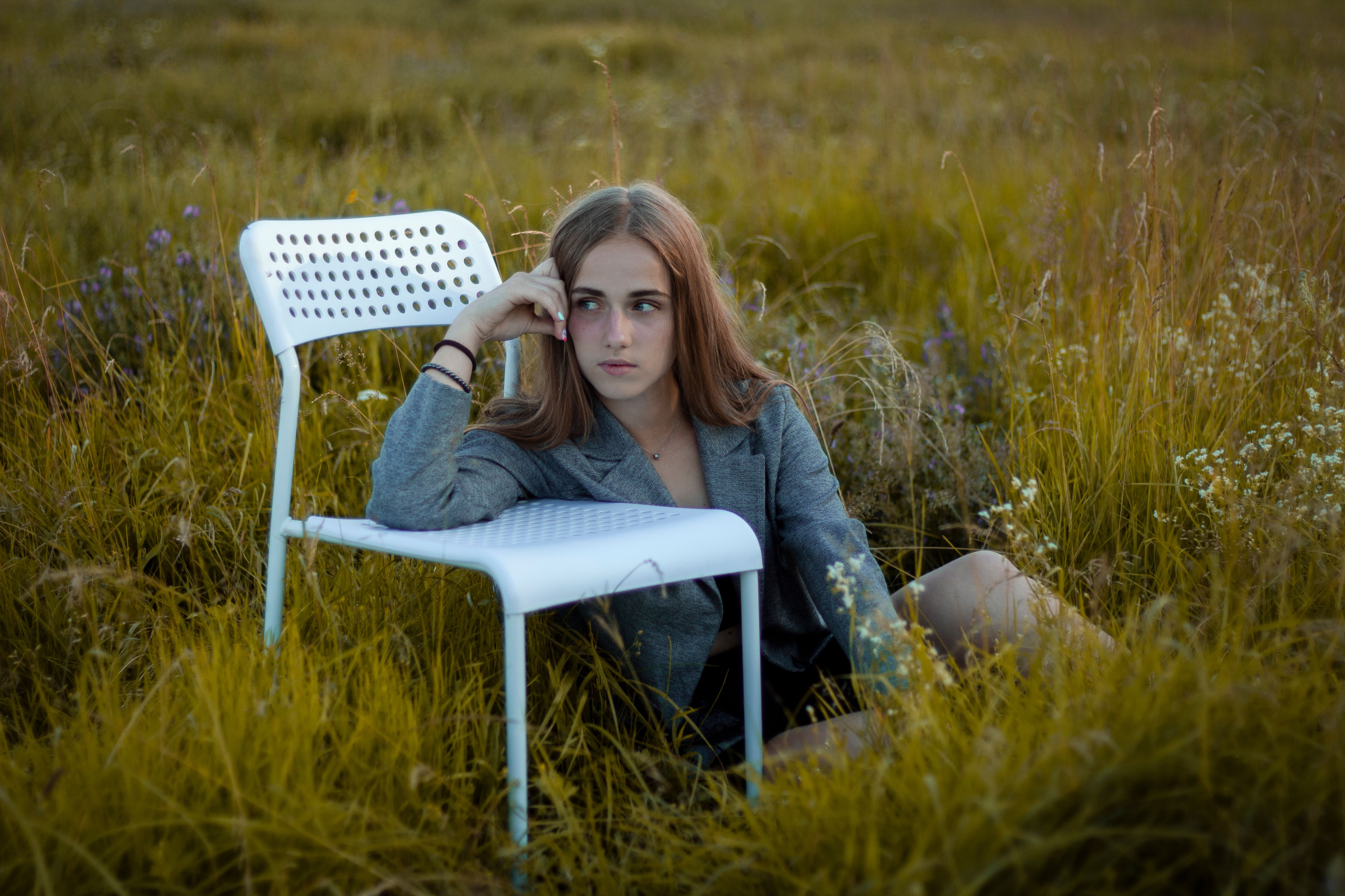 Woman Sitting on a Grass Field Next to a White Chair · Free Stock Photo