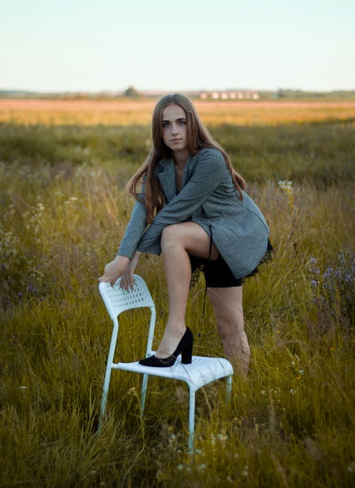 Free A Woman Stepping on a Chair while Posing in a Field Stock Photo