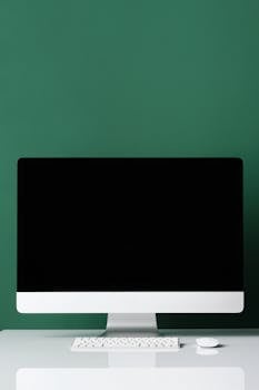 Minimalist setup of a desktop computer on a white table against a green wall, ideal for tech and design themes.