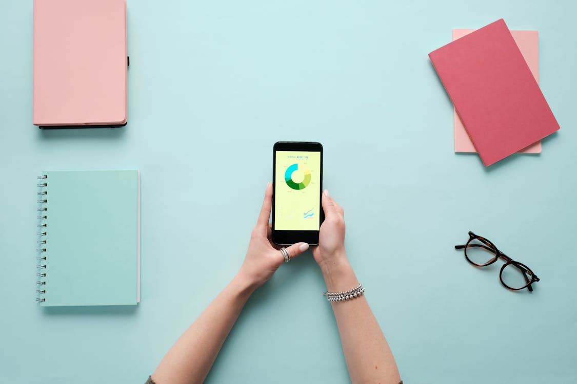 Hands holding a phone with analytics on the screen in front of a blue background.