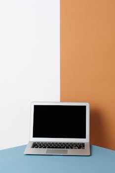 A laptop on a blue surface with a minimalist contrasting wall backdrop highlighting simplicity in design.