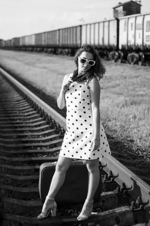 Free Elegant woman in polka dot dress posing on train tracks with suitcase, black and white photo. Stock Photo