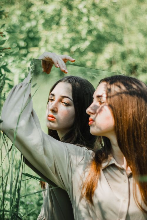 Free A thoughtful woman holds a mirror in a green garden, reflecting her serene expression. Stock Photo