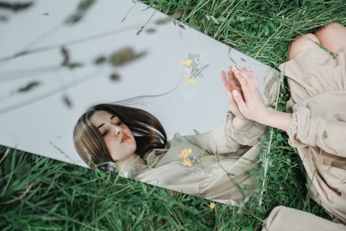 Free A woman in a beige dress is reflected in a mirror set on grass outdoors. Stock Photo